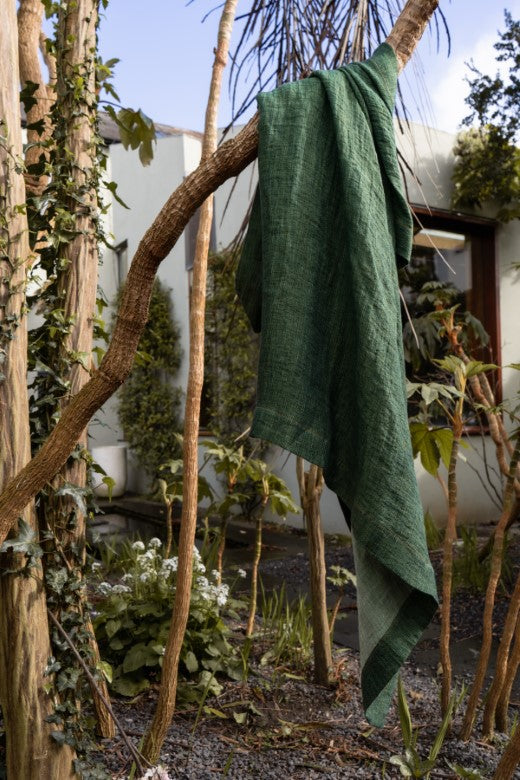 Grassy green, heavyweight Irish linen swim towel, artisan-woven with a textured finish, hanging outdoors in a garden.