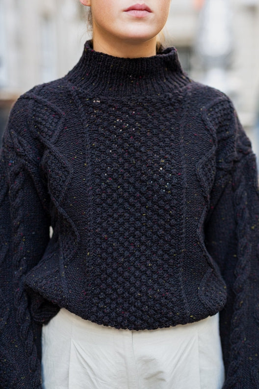 Hand-knit black merino wool Aran jumper with blackberry stitch, crafted by Irish artisans in a relaxed boxy fit.