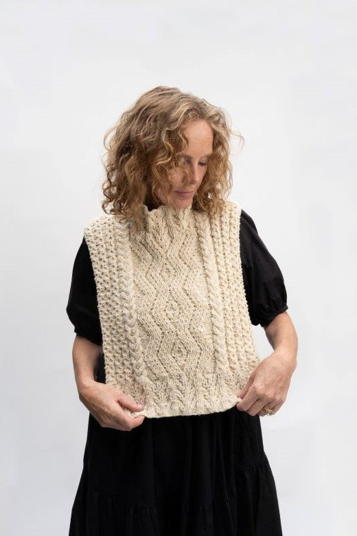 Cream-colored handknit Aran cable bib, crafted in Donegal by Irish artisans using premium wool with intricate textures.
