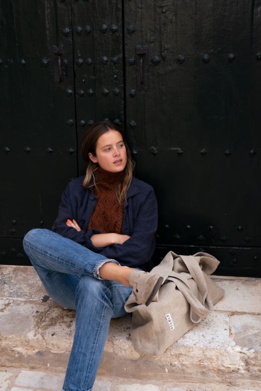 Hand-knit brown Aran cable bib by Irish maker Muriel, featuring intricate wool textures worn over a dark jacket.