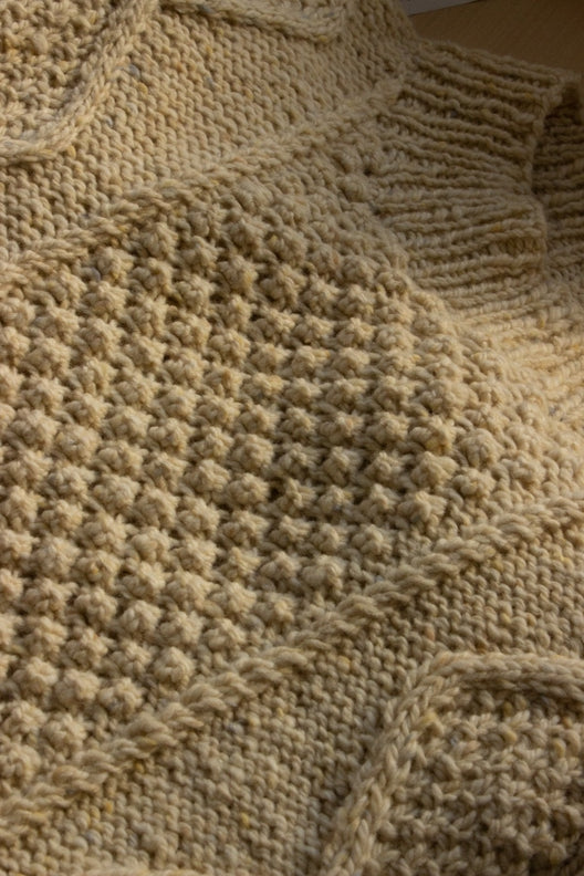 Cream-colored handknit merino wool Aran jumper featuring intricate blackberry stitch, crafted by Irish artisans.