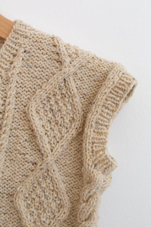 Hand-knitted Irish Aran vest in flecked Donegal merino wool featuring traditional cable knit patterns and ribbed trim.