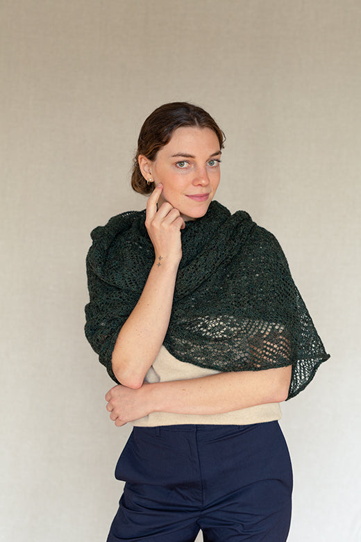 Woman wearing a peat green, artisan-knit alpaca lace shawl, handcrafted in Ireland with intricate traditional patterns.
