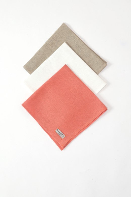 Three heavy-weight Irish linen napkins in coral, white, and natural beige, handmade in Ireland with a signature STABLE label.