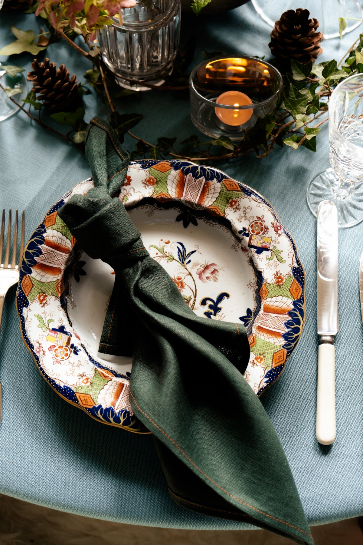 Dark green heavy-weight Irish linen napkin handmade in Ireland, styled on a decorative plate with a blue tablecloth.