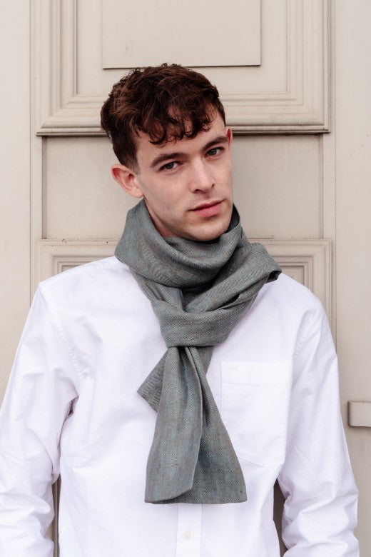Model wearing a warm turquoise Irish linen scarf with frayed edges, handcrafted by skilled Irish makers from sustainable flax.