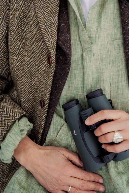 Sage green Irish linen smock shirt with high collar, worn under a herringbone tweed jacket with binoculars.