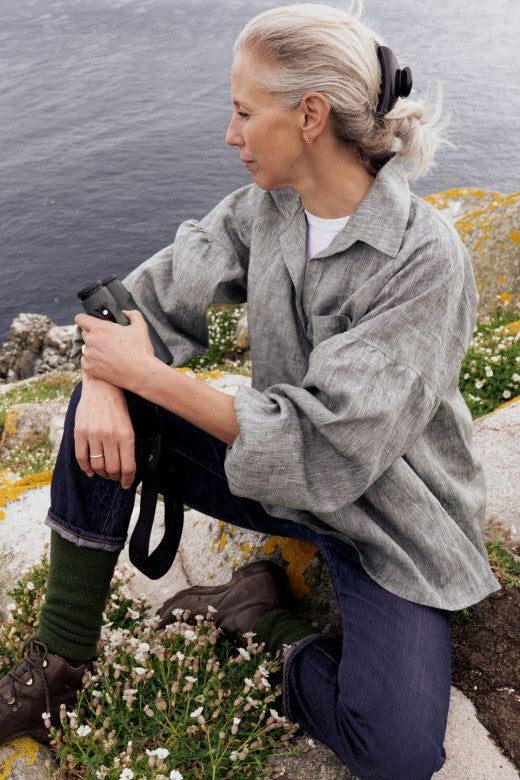 Woman wearing a grey Irish linen work shirt, featuring a loose smock design, high collar, and chest pocket, outdoors.