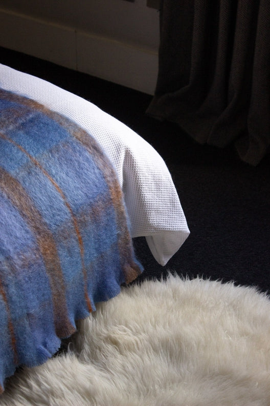 Luxurious, soft cream Irish sheepskin rug handcrafted by local artisans, displayed on a bedroom floor beside a blue plaid throw.