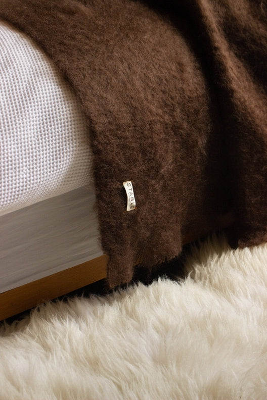 Luxurious dark brown Irish wool throw draped over a soft, cream-colored sheepskin rug, crafted by skilled Irish artisans.