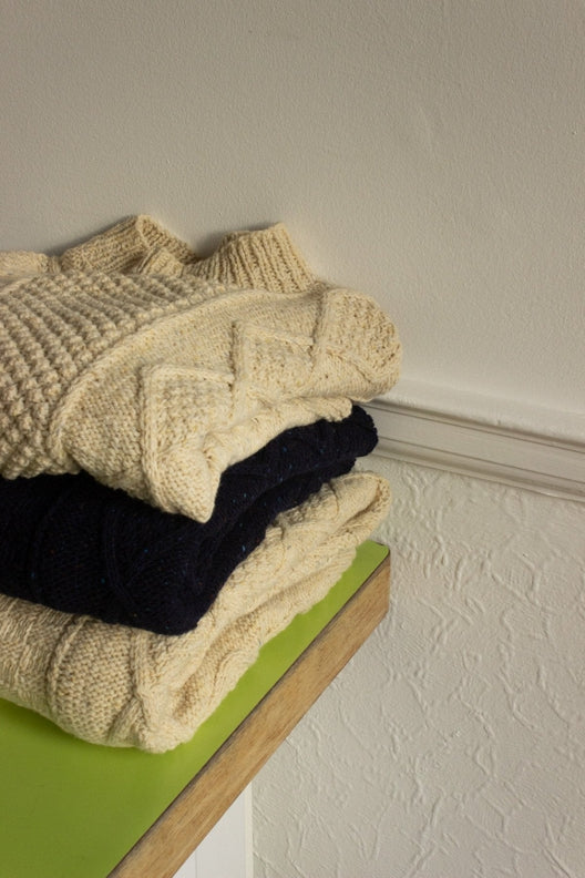 Stack of soft merino wool Aran jumpers, artisan-made in Ireland featuring traditional cable and diamond stitch patterns.