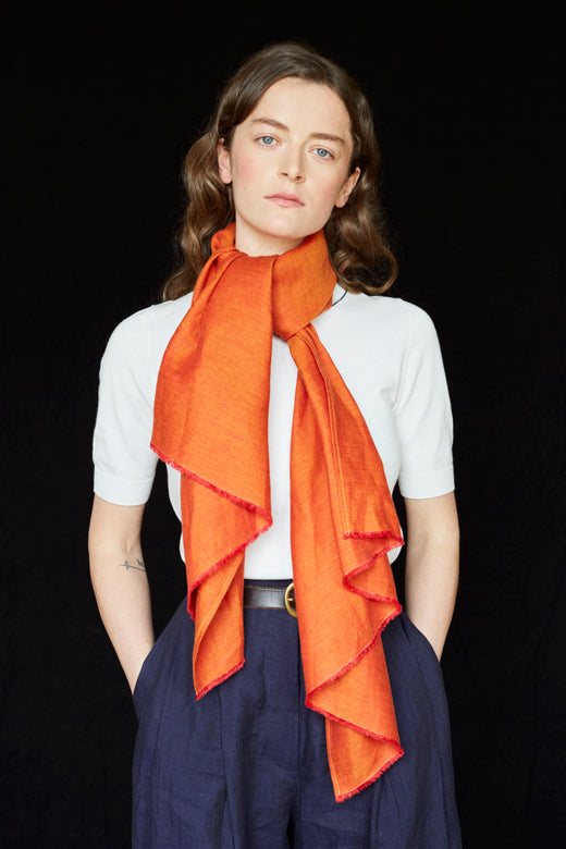 Model wearing a vibrant orange herringbone Irish linen scarf, handcrafted by skilled makers using high-quality textiles.